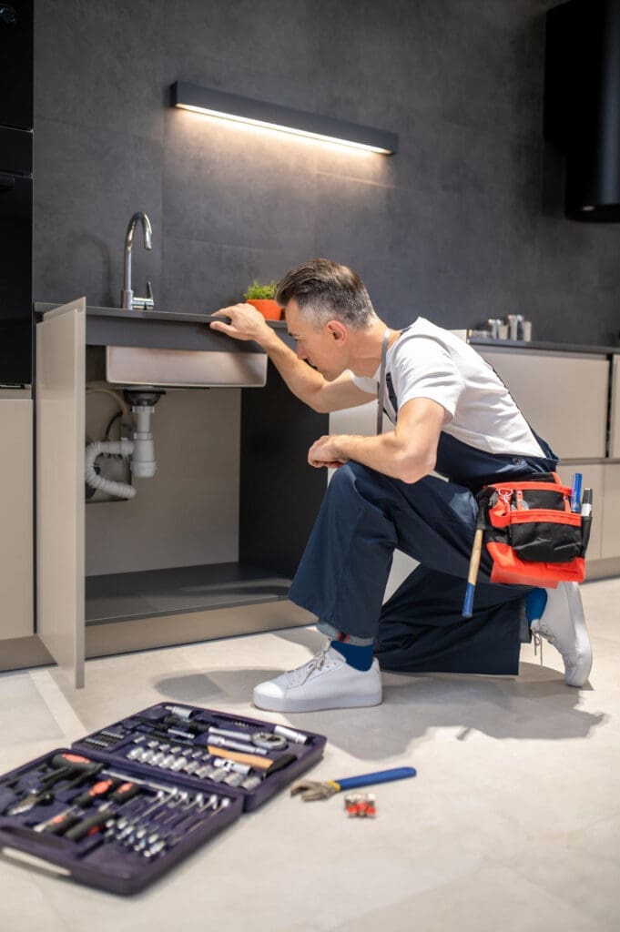 Emergency plumber inspecting pipes under a kitchen sink during repair