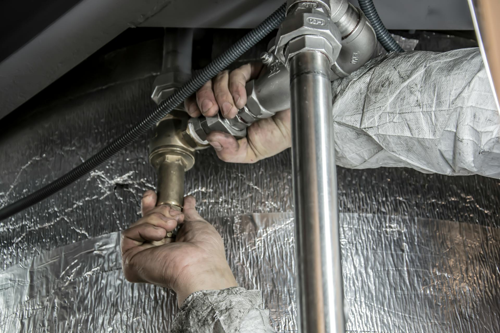 Close-up of an emergency plumber repairing household pipes under a sink